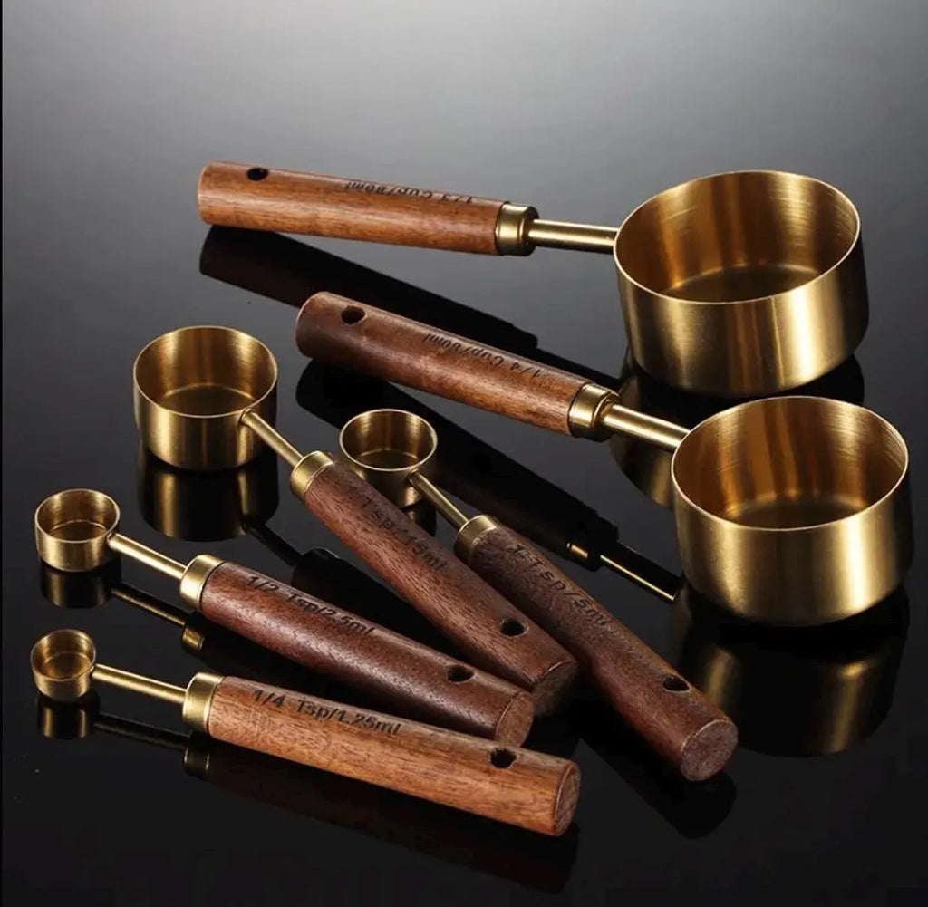 Set of brass measuring cups with wooden handles on a reflective black surface