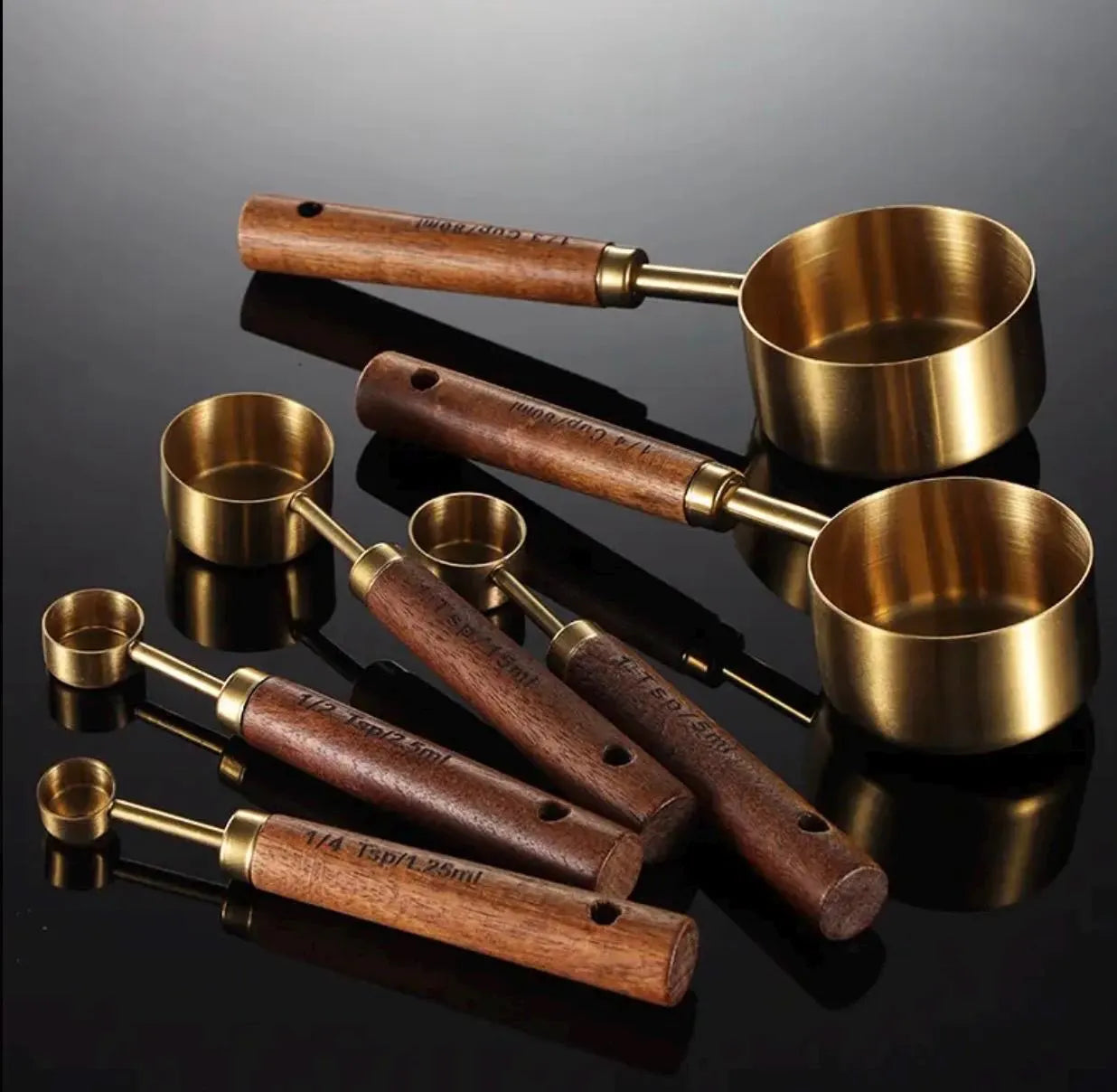Set of brass measuring cups with wooden handles on a reflective black surface