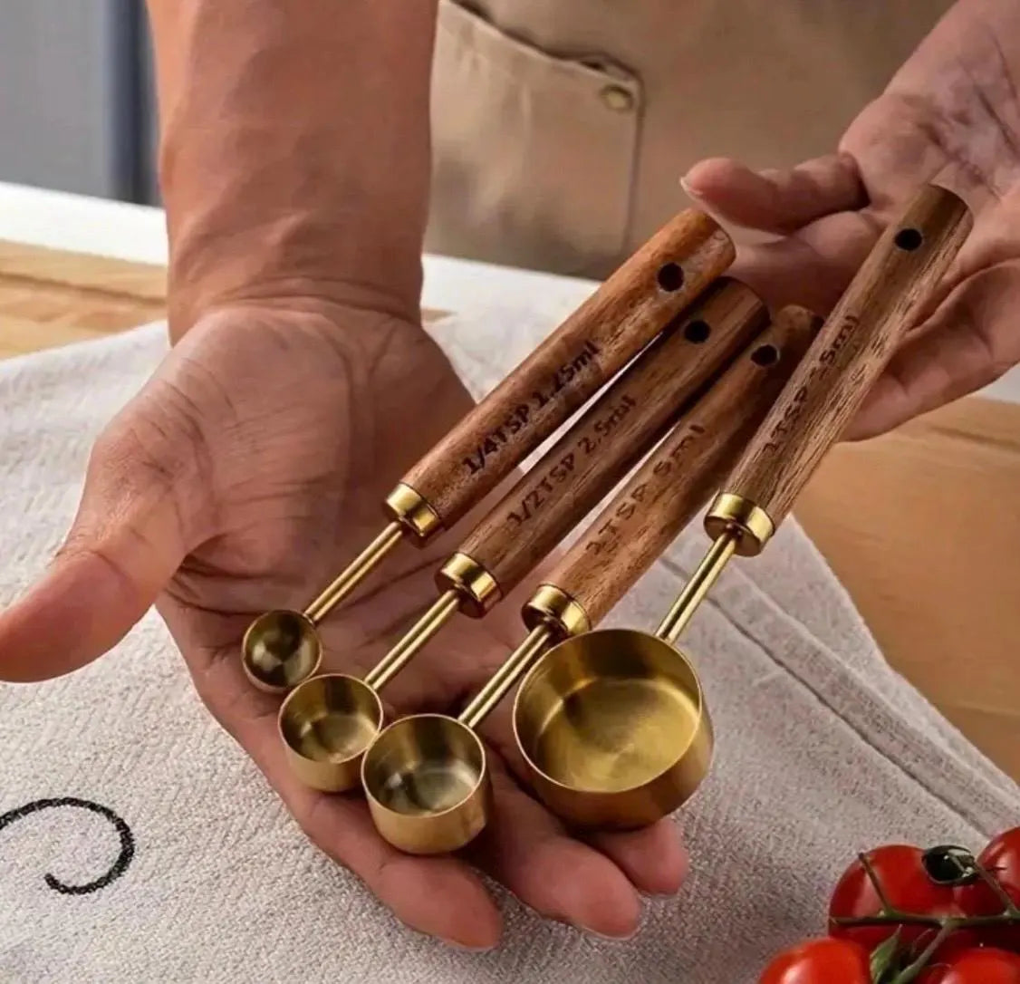 Set of brass measuring cups with wooden handles held by a person, with a blurred background.