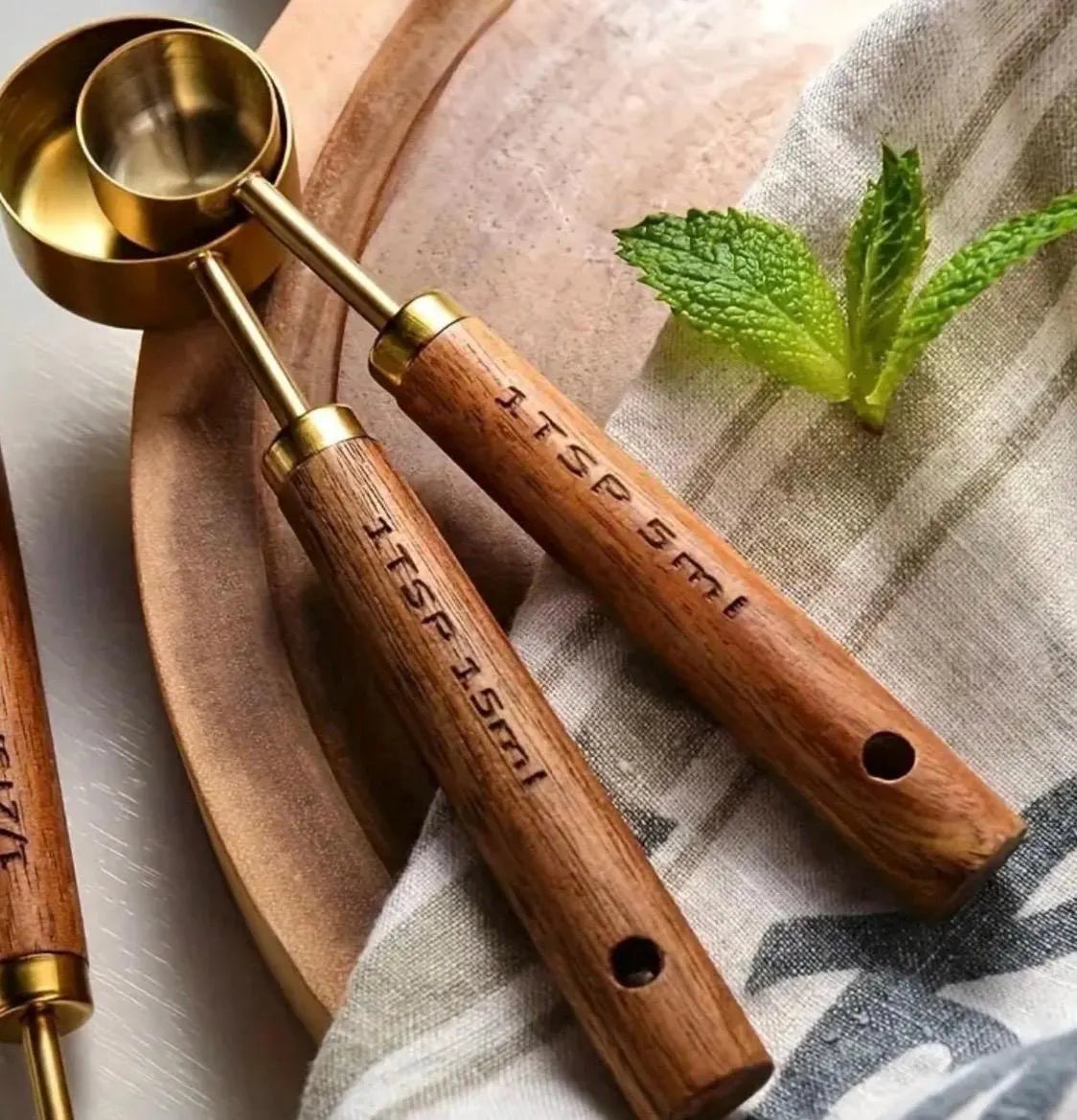 Wooden measuring spoons with gold accents on a textured surface with mint leaves.