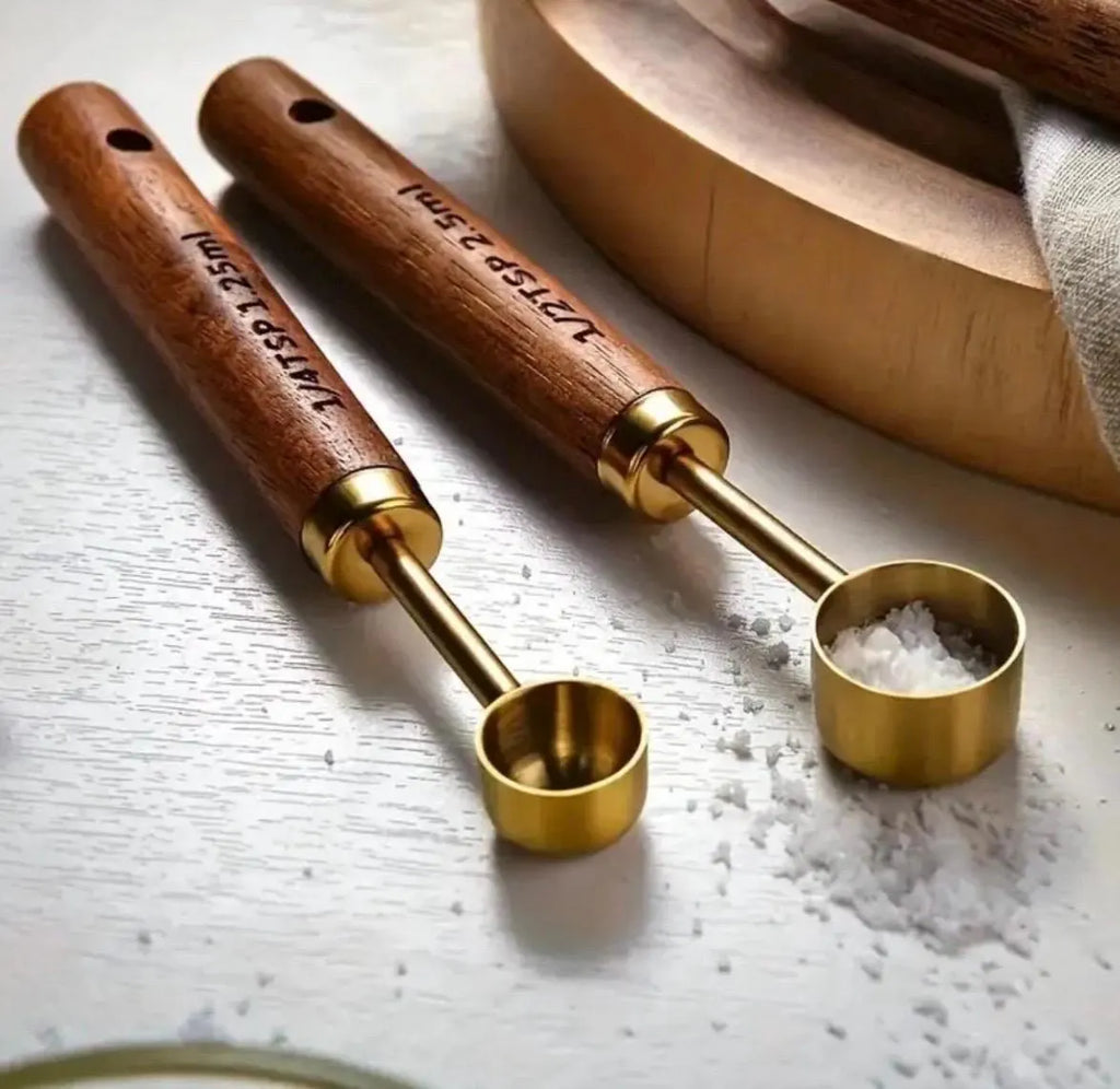 Two wooden-handled brass measuring spoons on a light surface with salt.