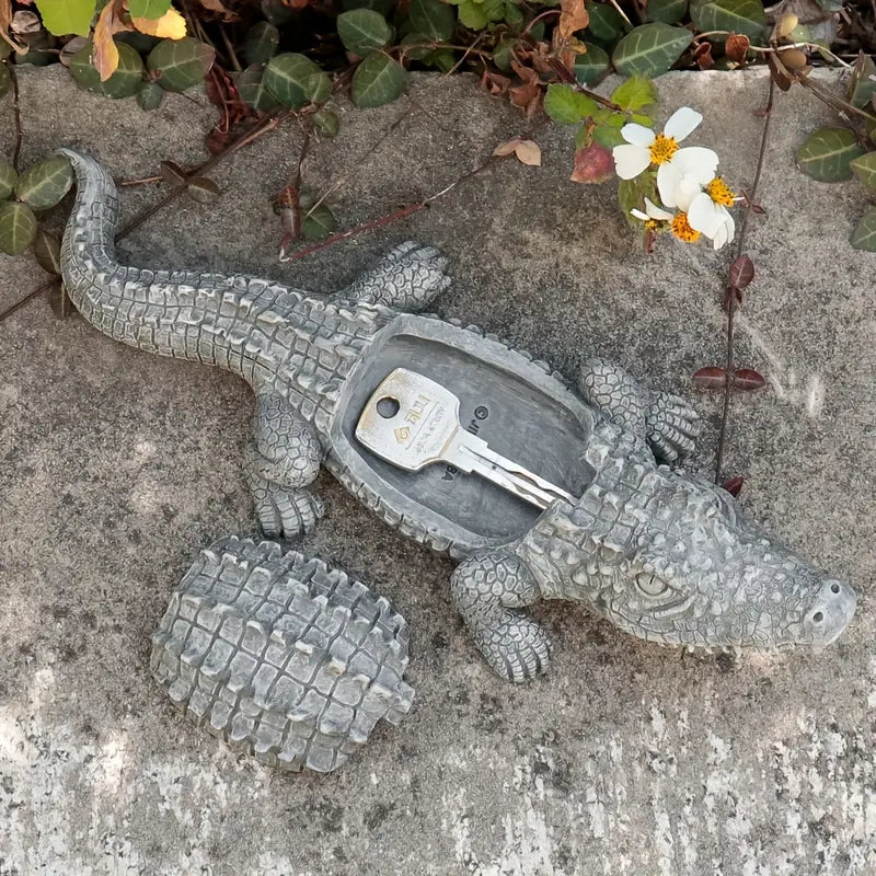 Decorative alligator-shaped key holder on a concrete surface with flowers in the background