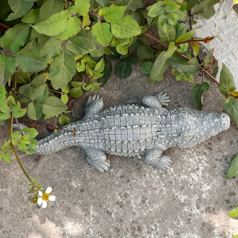 Toy alligator on a sandy surface with green leaves and flowers