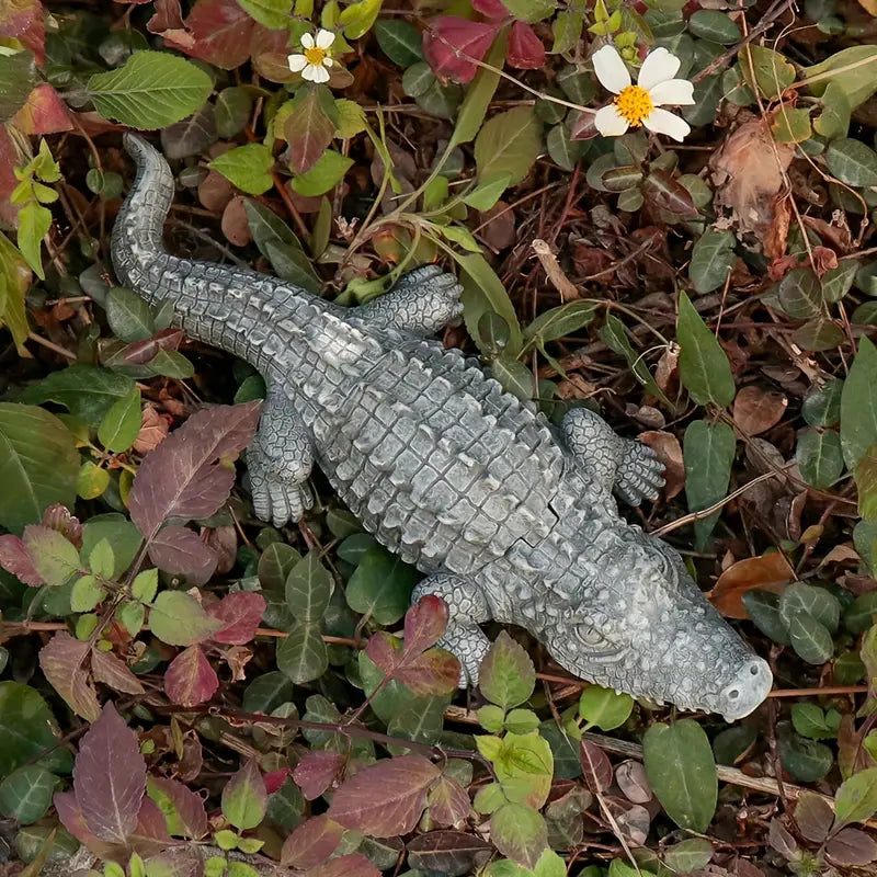 Gray alligator toy on a bed of leaves and small flowers