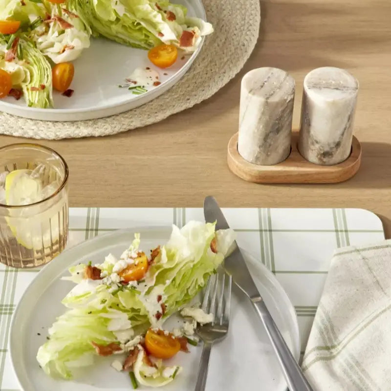 Wedge salad on a plate with a glass of water and salt and pepper shakers on a wooden table.