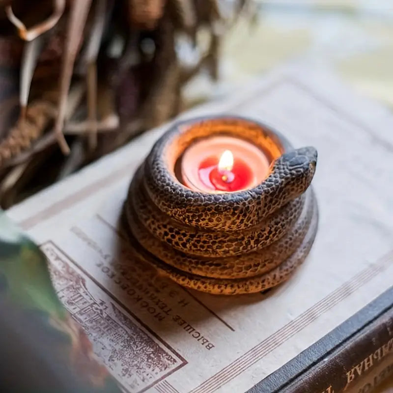 Candle holder shaped like a snake with a lit candle inside, placed on an open book.